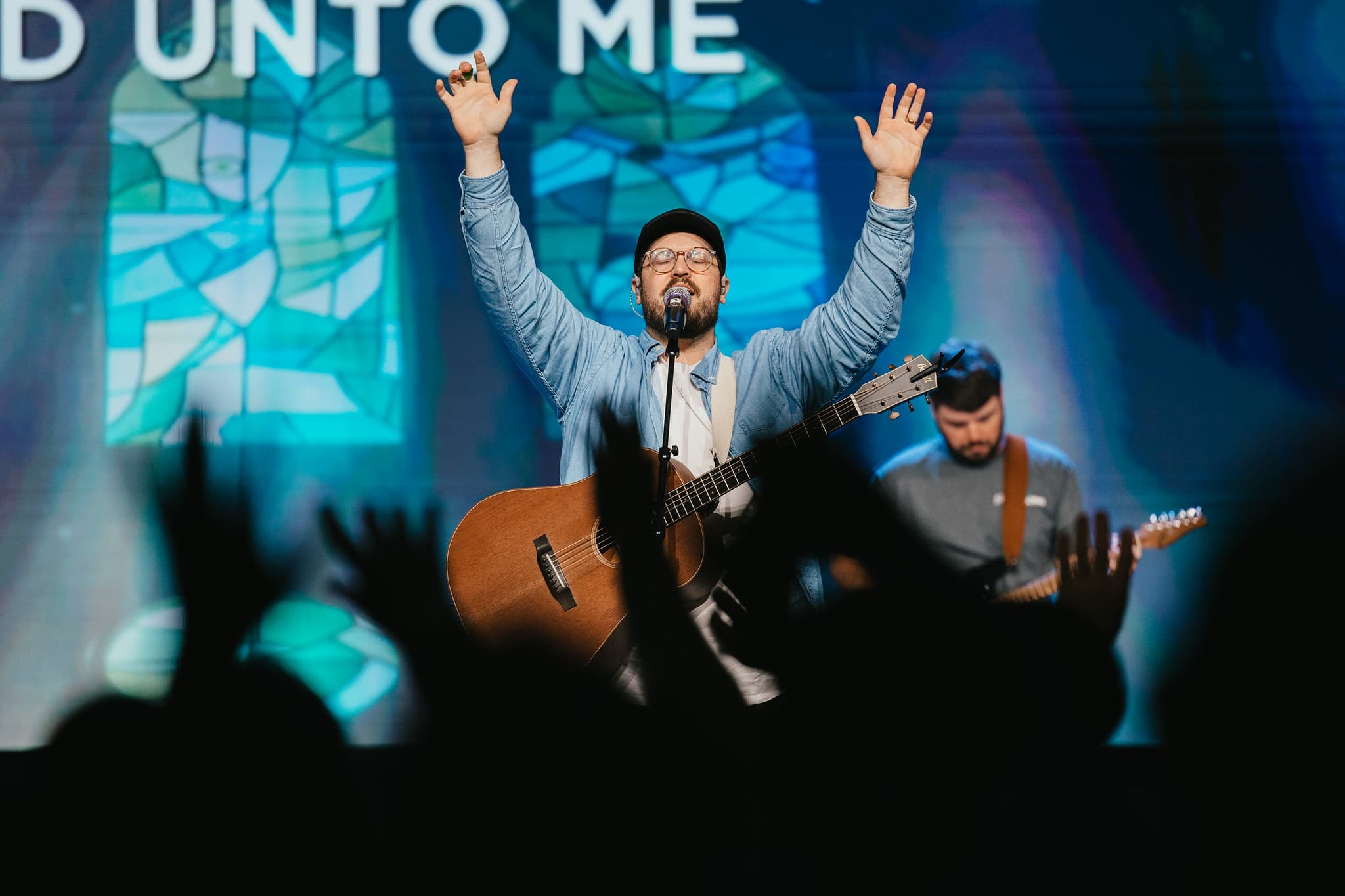 Joe Richardson leading worship, hands raised, with the congregation worshipping in the foreground